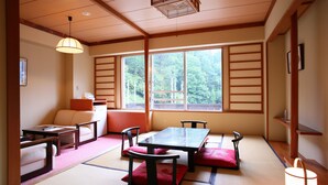 A traditional Japanese room with tatami flooring, a low table with cushions, and a view of a forest through large windows. - Nozawa Grand Hotel (Nozawaonsen)