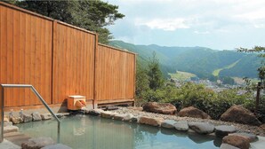 A wooden cabin with a hot spring bath surrounded by rocks and a view of a valley. - Nozawa Grand Hotel (Nozawaonsen)