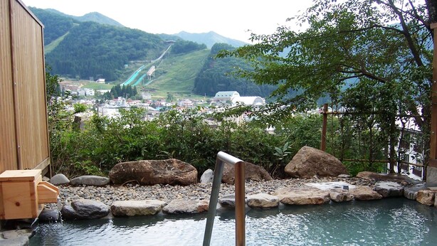 A traditional Japanese onsen with a view of a town and mountains in the background. - Nozawa Grand Hotel (Nozawaonsen)