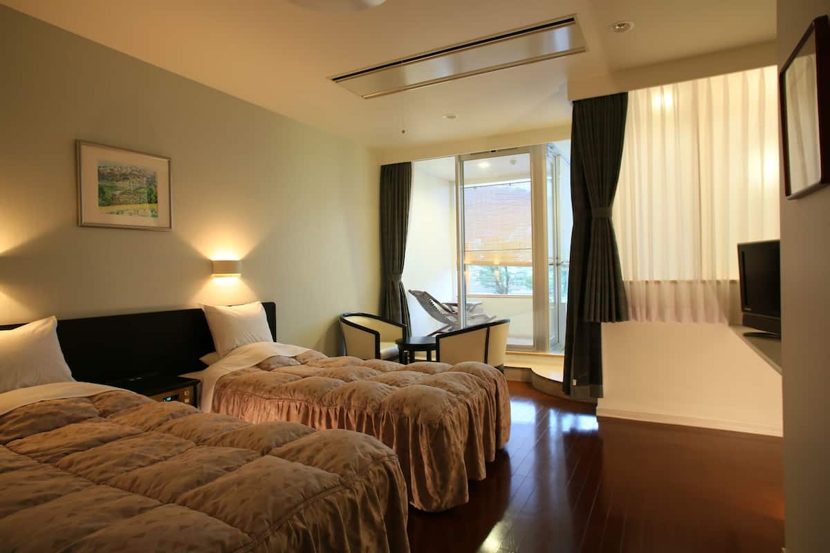 A hotel room with two beds, a desk, a chair, a TV, and a window with curtains.