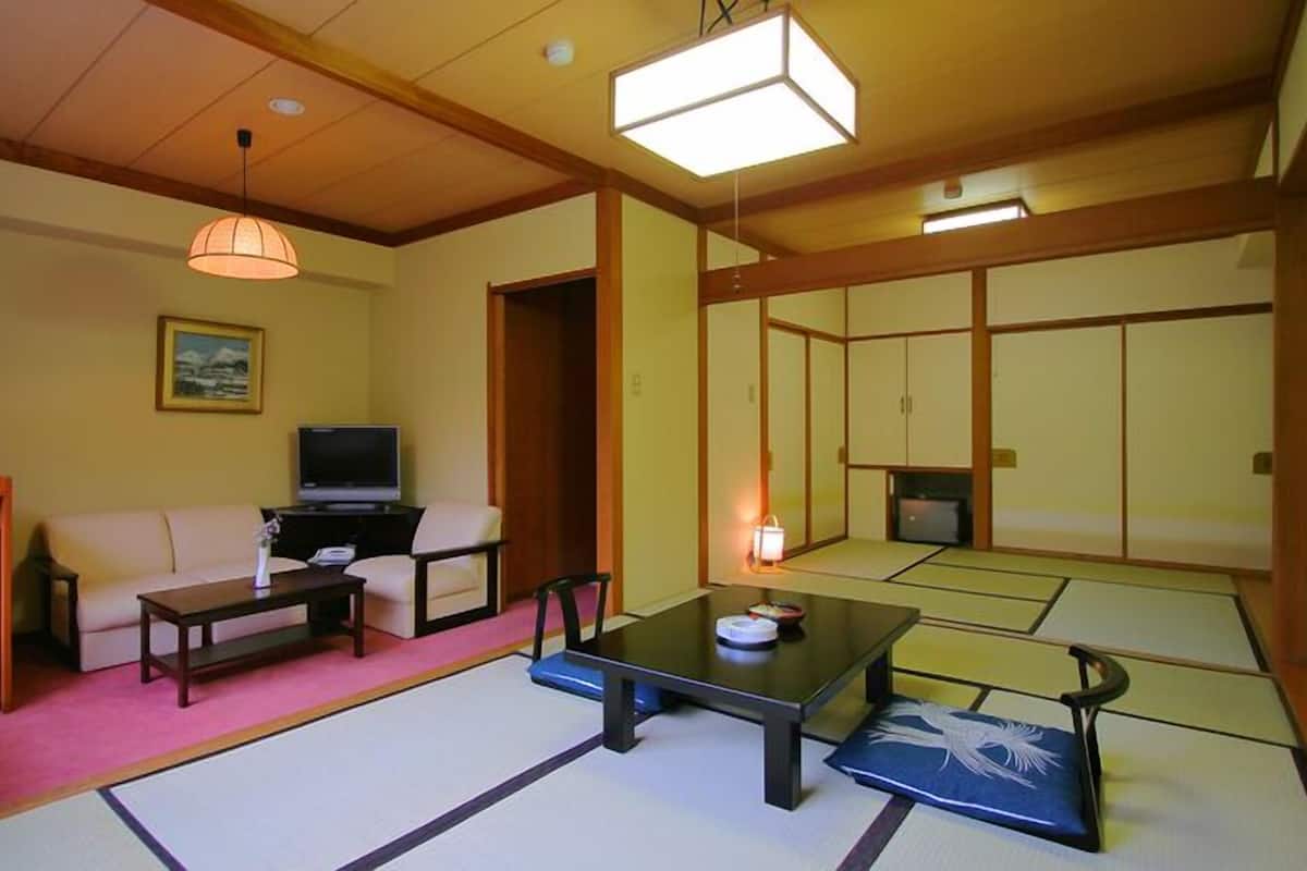 A traditional Japanese-style room with tatami flooring, a low table, a sofa, a television, and sliding doors.
