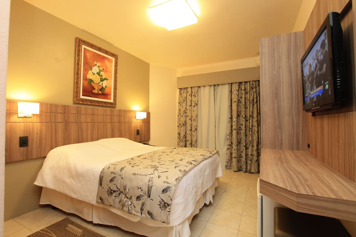 Una camera d'albergo con un letto grande, una TV a parete e un quadro appeso.
