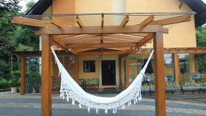 A hammock under a wooden pergola with a building in the background. - Pousada Águia Branca (Gramado)