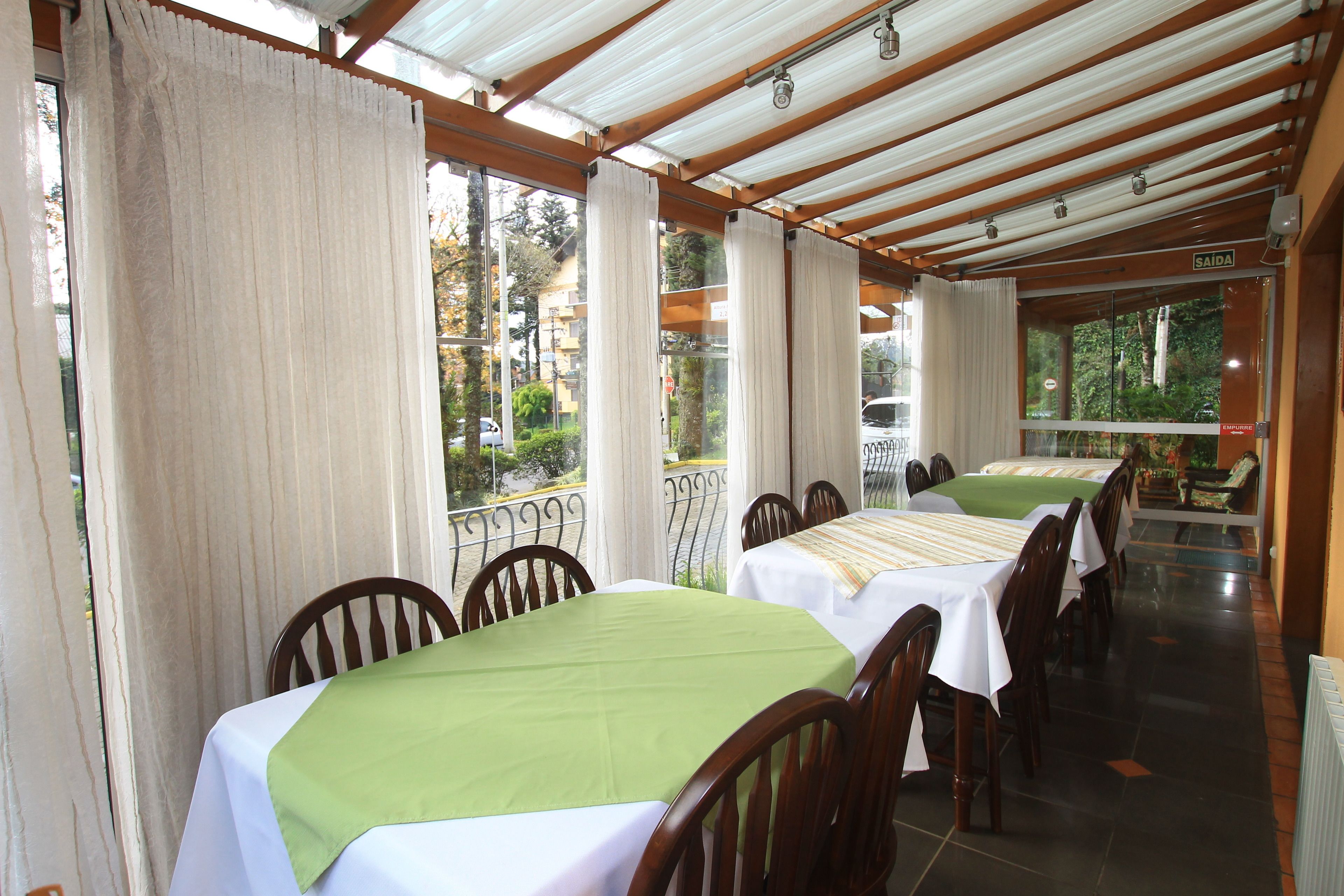 Un restaurante con varias mesas cubiertas con manteles verdes, sillas de madera y vistas al exterior a través de amplios ventanales.