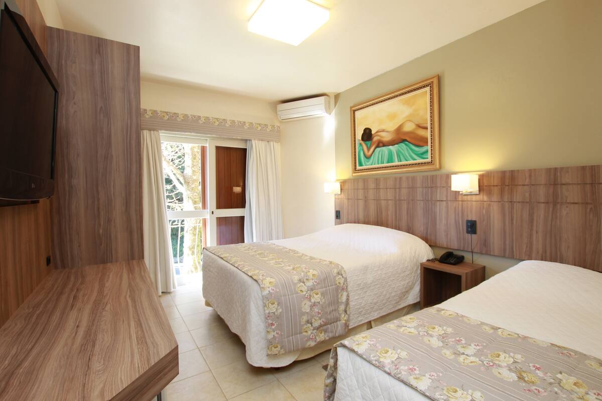 Una camera d'albergo con due letti, un armadio in legno, un quadro appeso al muro e un balcone con tende.