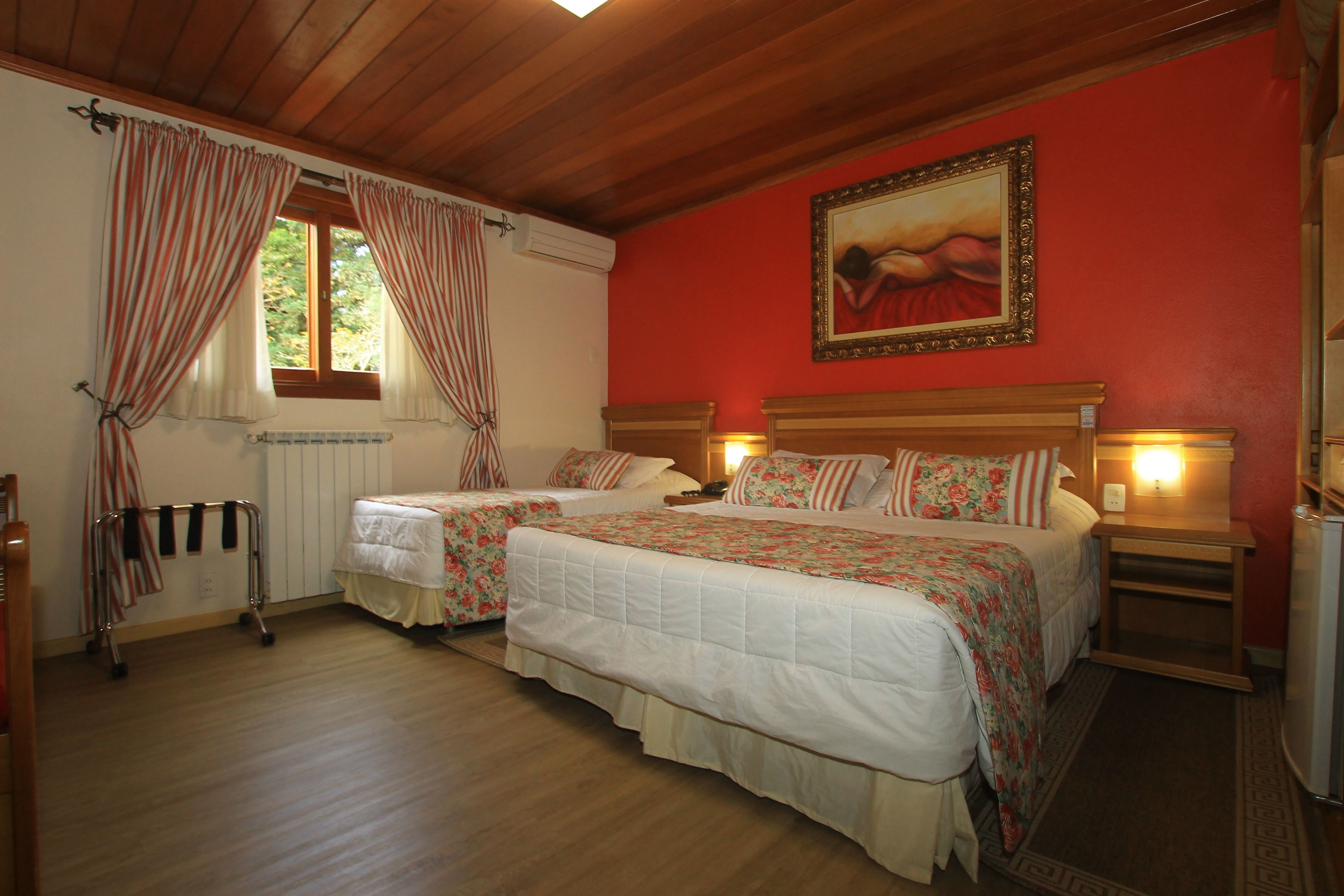 Un dormitorio con dos camas, suelo de madera, un radiador, una ventana con cortinas, un cuadro en la pared y lámparas de noche.
