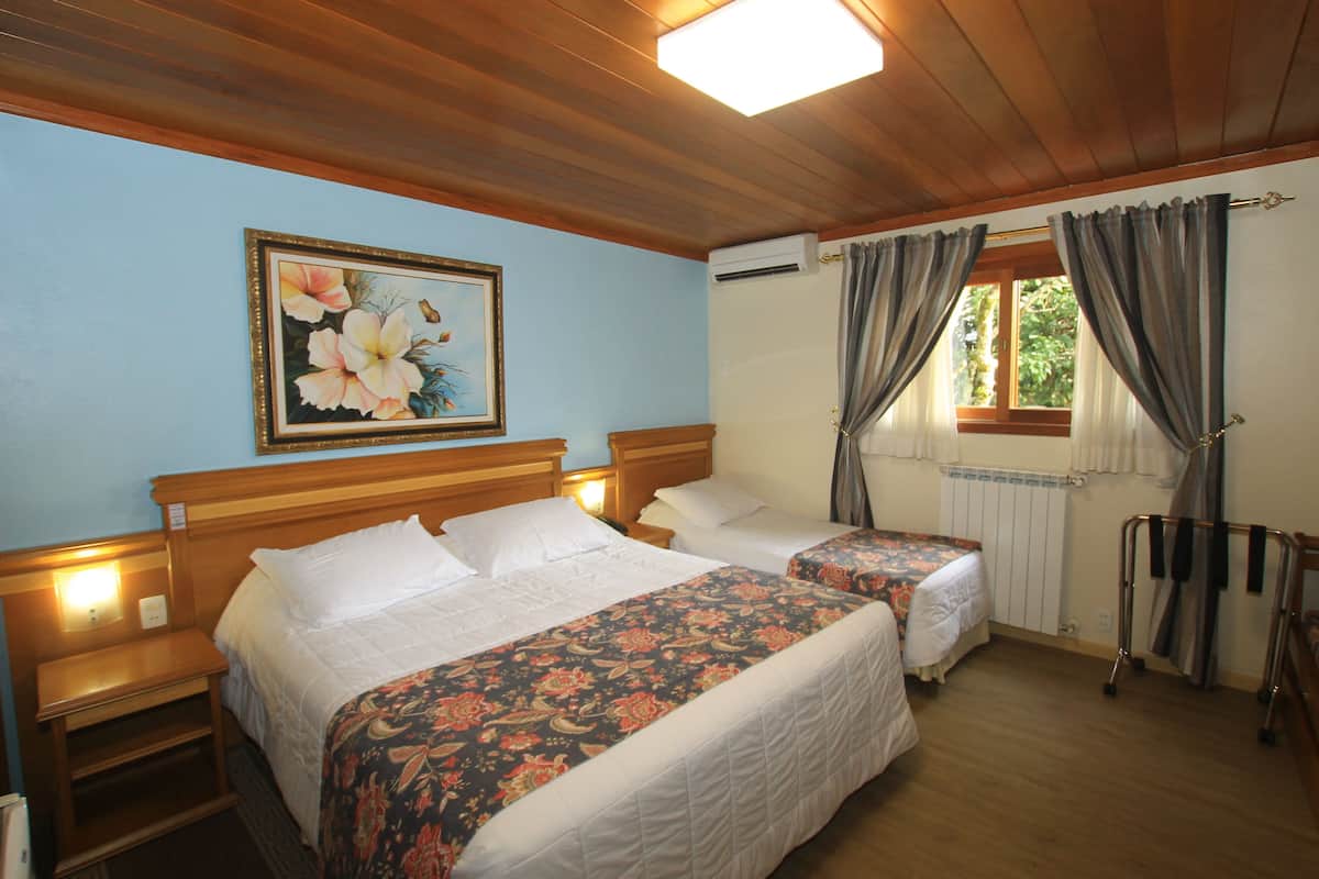 Una camera d'albergo con due letti, testiere in legno, un comodino e una tenda da finestra, oltre a un condizionatore d'aria.