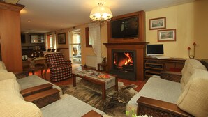 A cozy living room with a fireplace, a television, and comfortable seating. - Pousada Águia Branca (Gramado)
