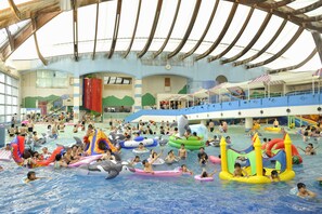 Una amplia piscina interior con diversos juguetes inflables y un techo alto con vigas de madera.
