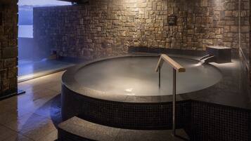 Relax in a serene hot tub surrounded by a stone wall, complete with a circular tub and wooden handrail.