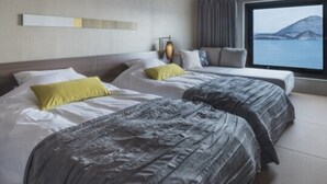 Une chambre d’hôtel avec deux lits, une grande fenêtre donnant sur la mer et un design moderne au niveau du plafond.
