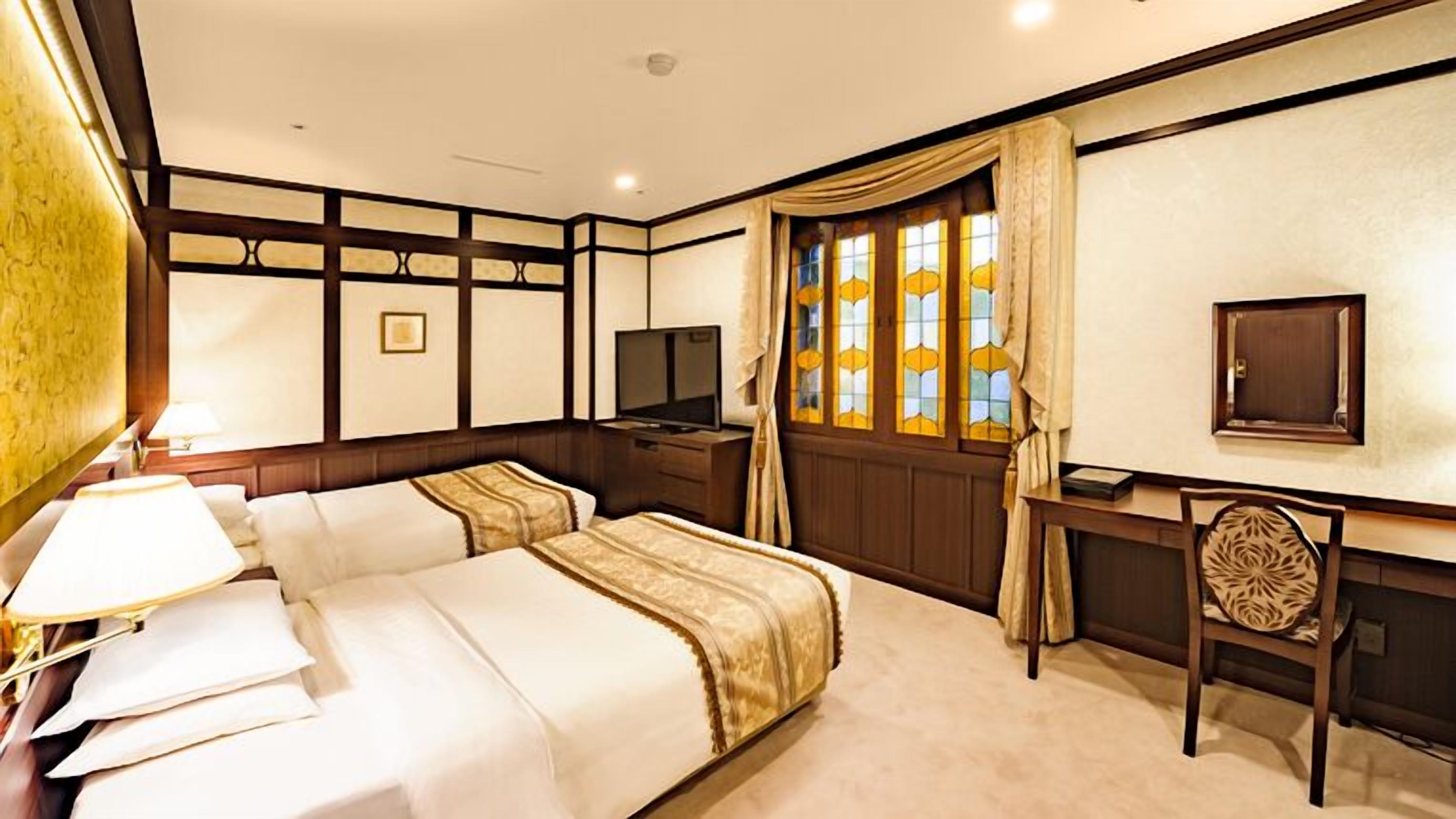 Een hotelkamer met een bed, bureau, stoel, televisie en een raam met gordijnen.
