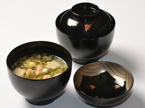 Tres tazones negros con superficie reflectante, uno contiene sopa transparente con verduras y carne, y los otros dos están vacíos.