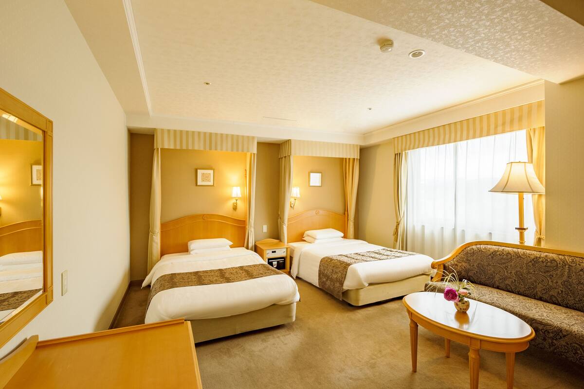 Ein Hotelzimmer mit zwei Betten, einem Schlafsofa, einem kleinen Tisch und einem Spiegel.