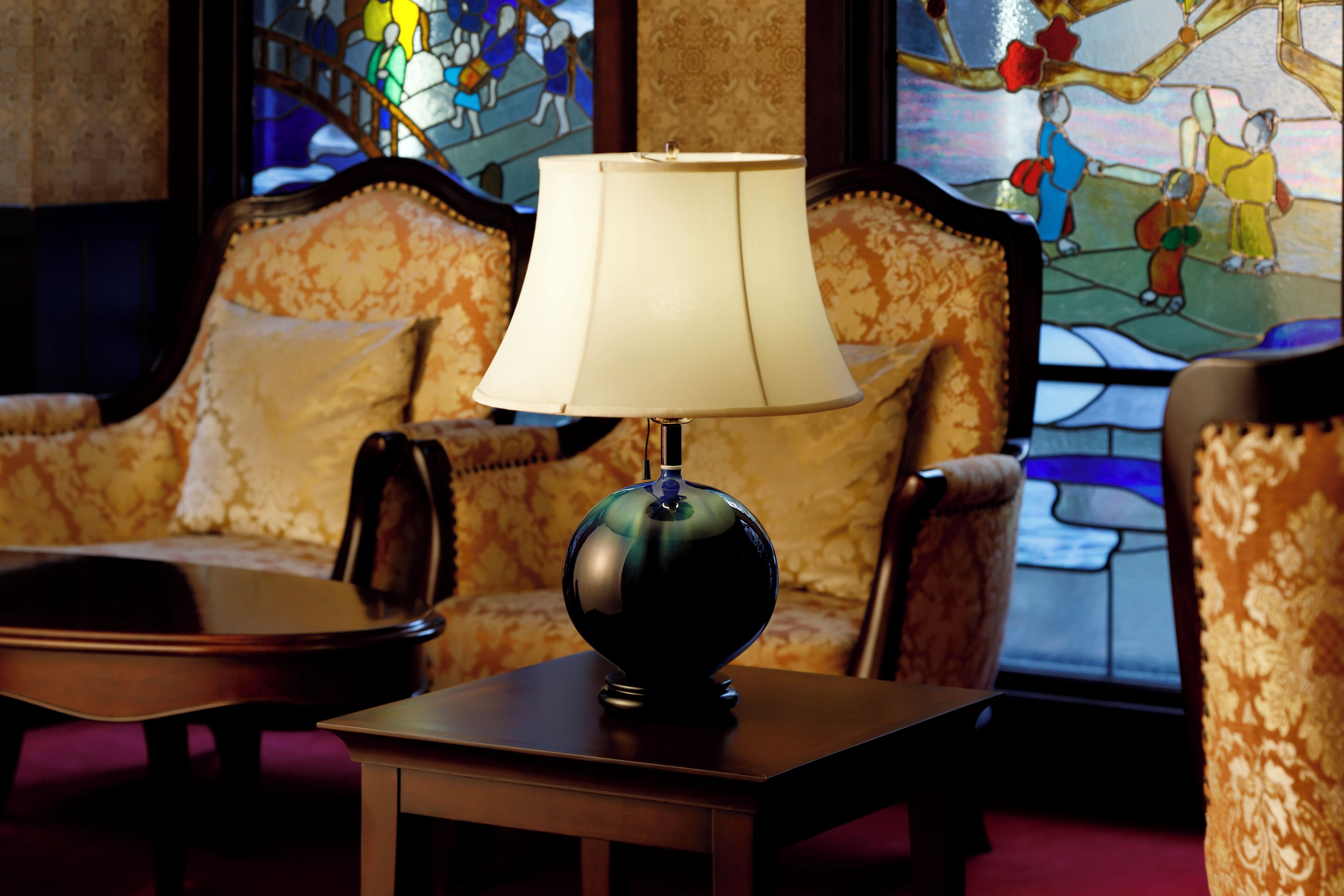 A lamp on a table, a sofa, and a stained glass window in a room.