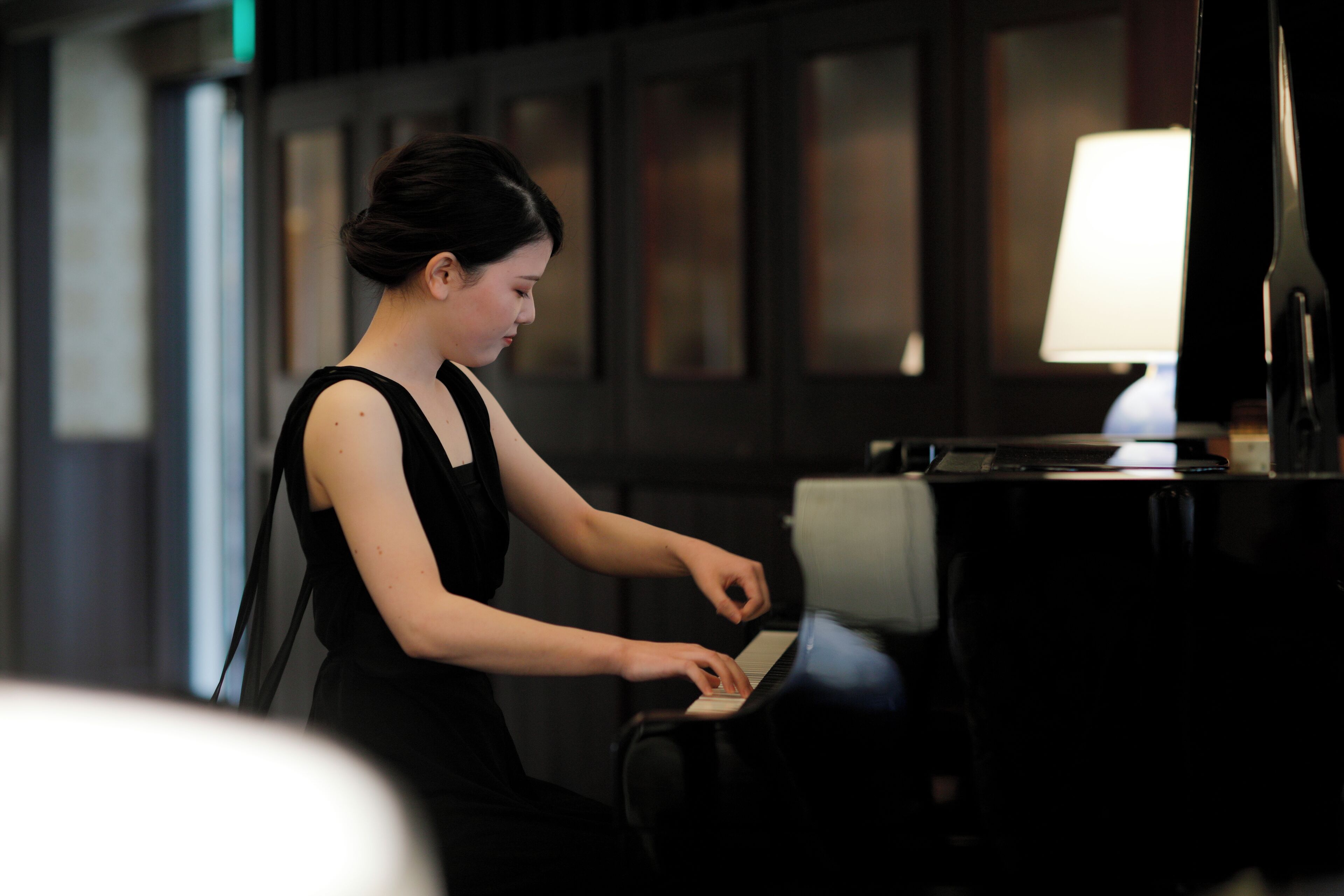 A person playing a piano in a dimly lit room with a lamp on a table.