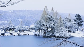 A snow-covered landscape with a traditional Japanese pavilion by a lake.