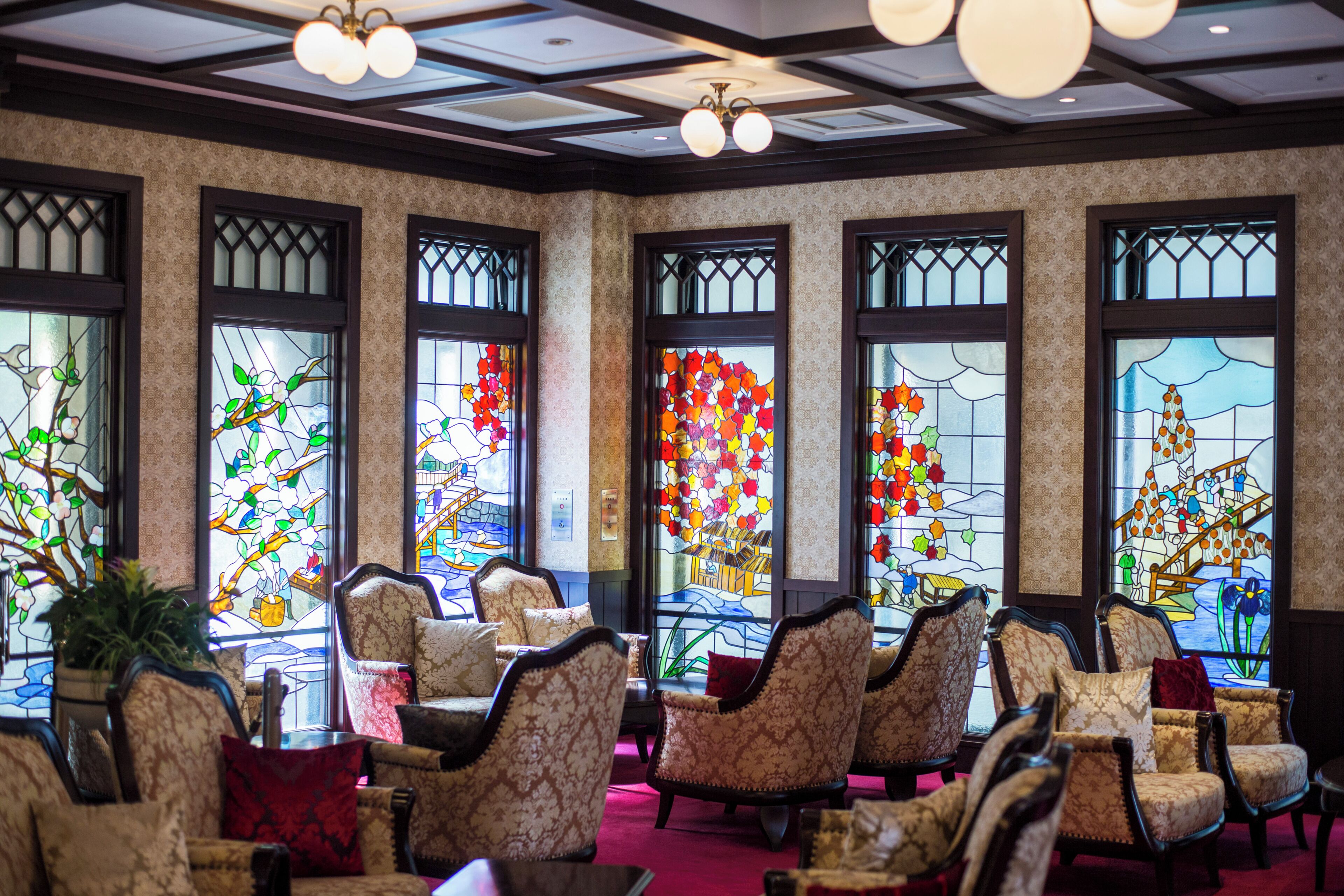 Un hall d’hôtel avec des fauteuils à motifs, de grandes fenêtres à vitraux et un plafond orné d’un motif en réseau.