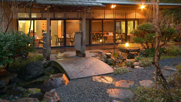 A traditional Japanese-style building with a covered outdoor seating area, stone pathway, and surrounding garden.