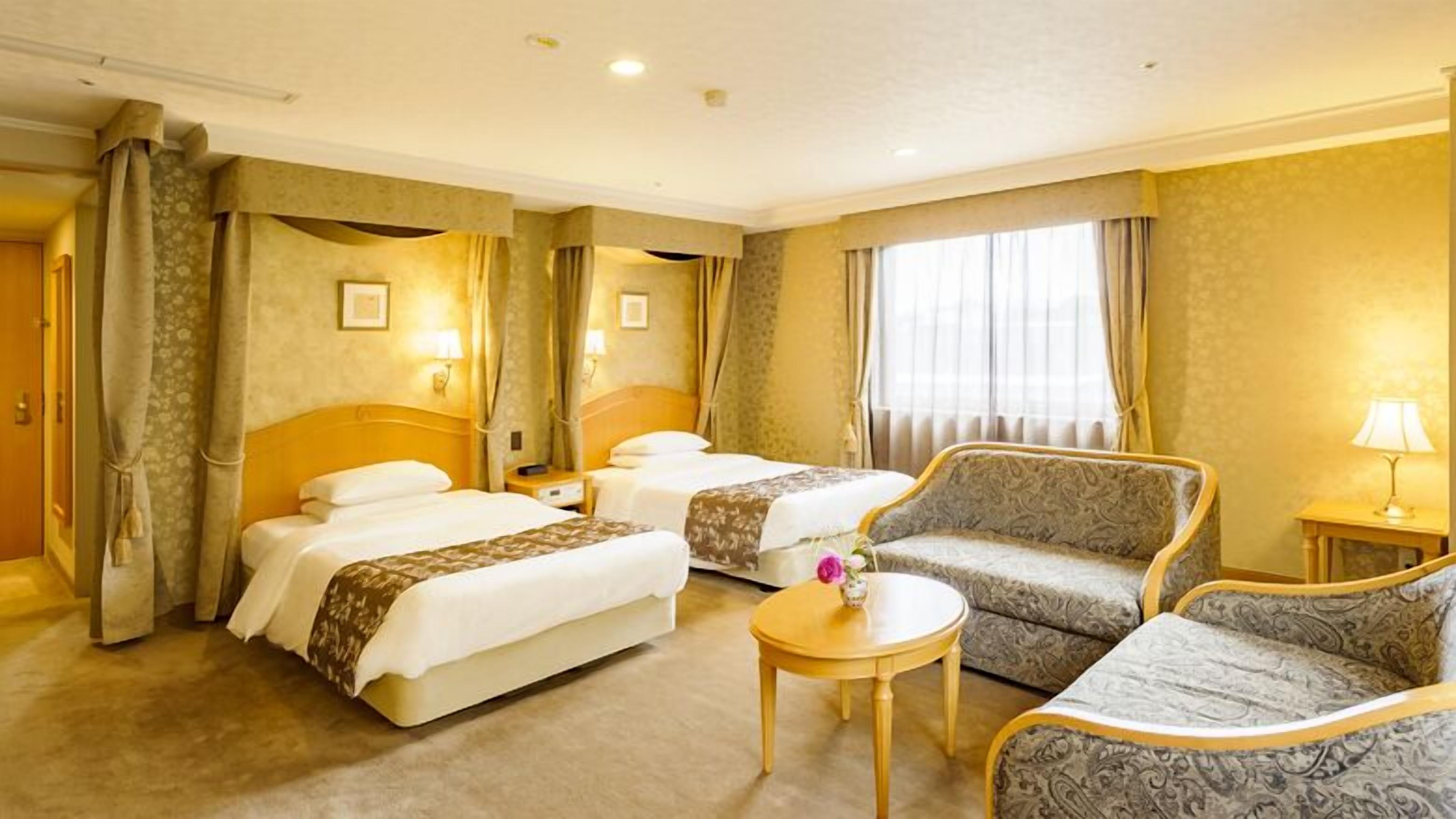 Een hotelkamer met twee bedden, een bank, een klein tafeltje en een lamp.