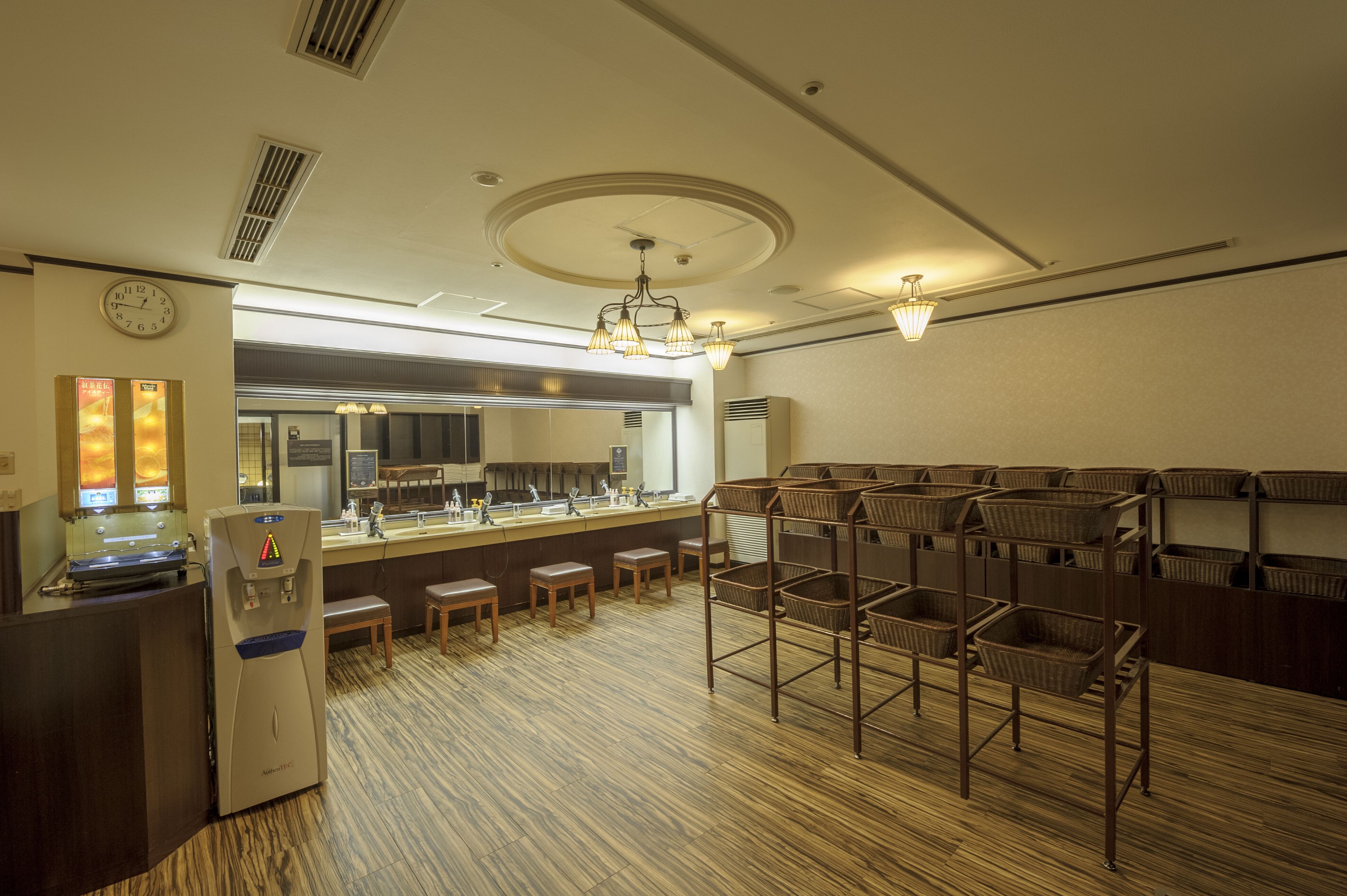 A hotel lobby with a reception desk, a clock, a water dispenser, and a seating area with wicker baskets.