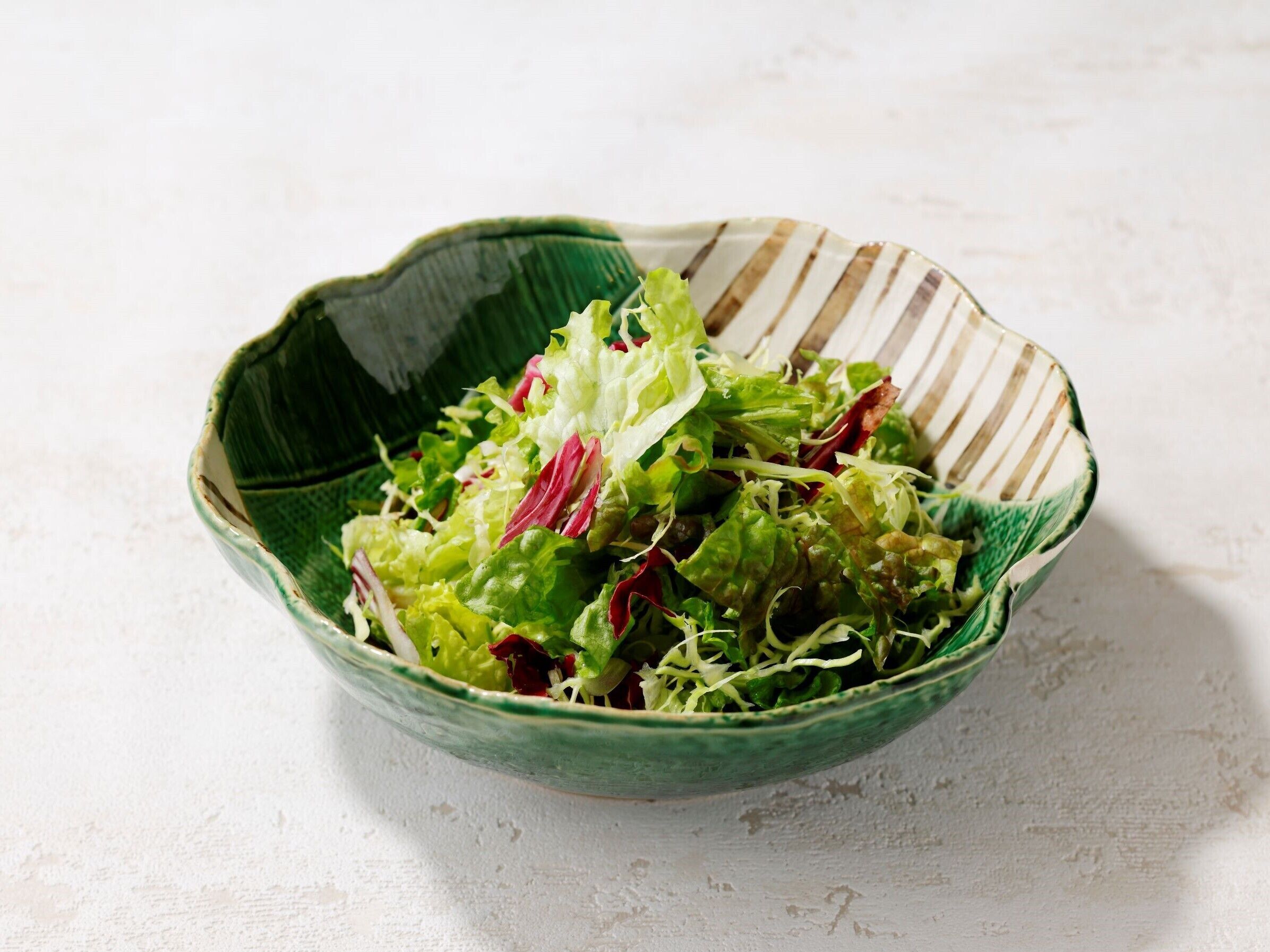 Een kom met een gemengde salade van groene en rode bladeren op een witte ondergrond.