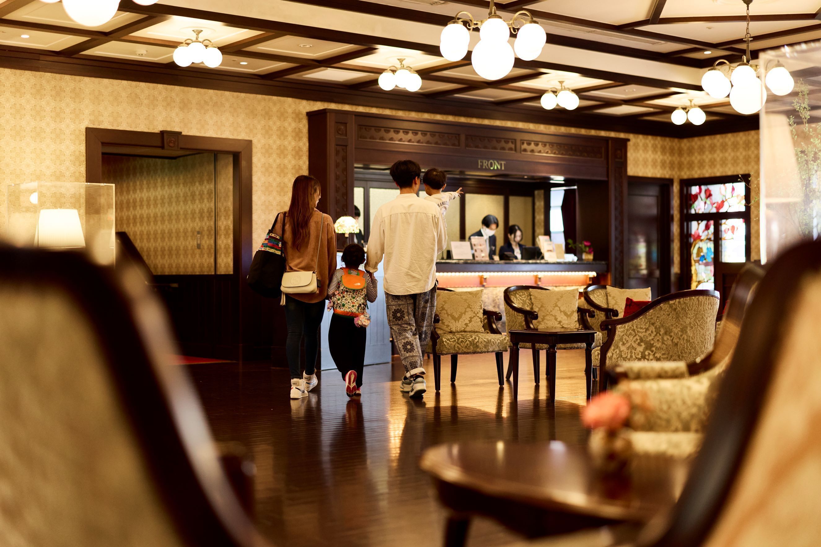 A hotel lobby with a reception desk, patterned wallpaper, and a chandelier.