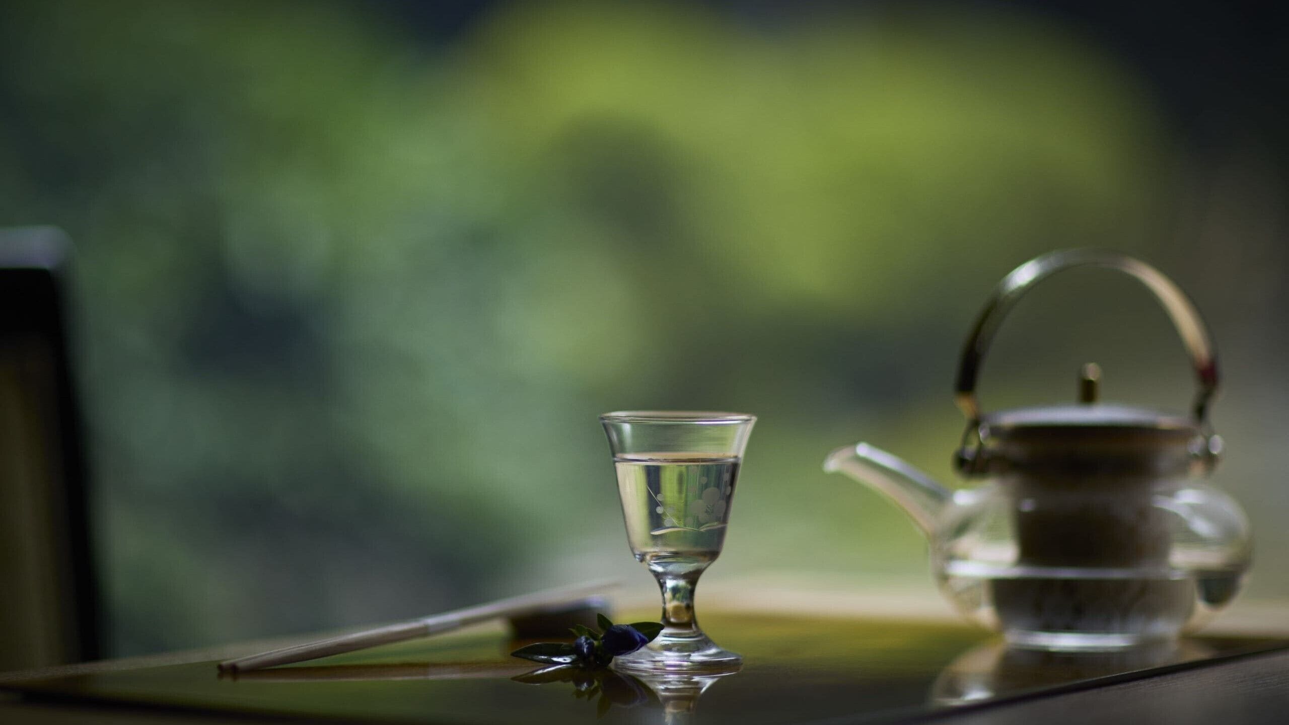 A clear glass cup and a teapot on a reflective surface.