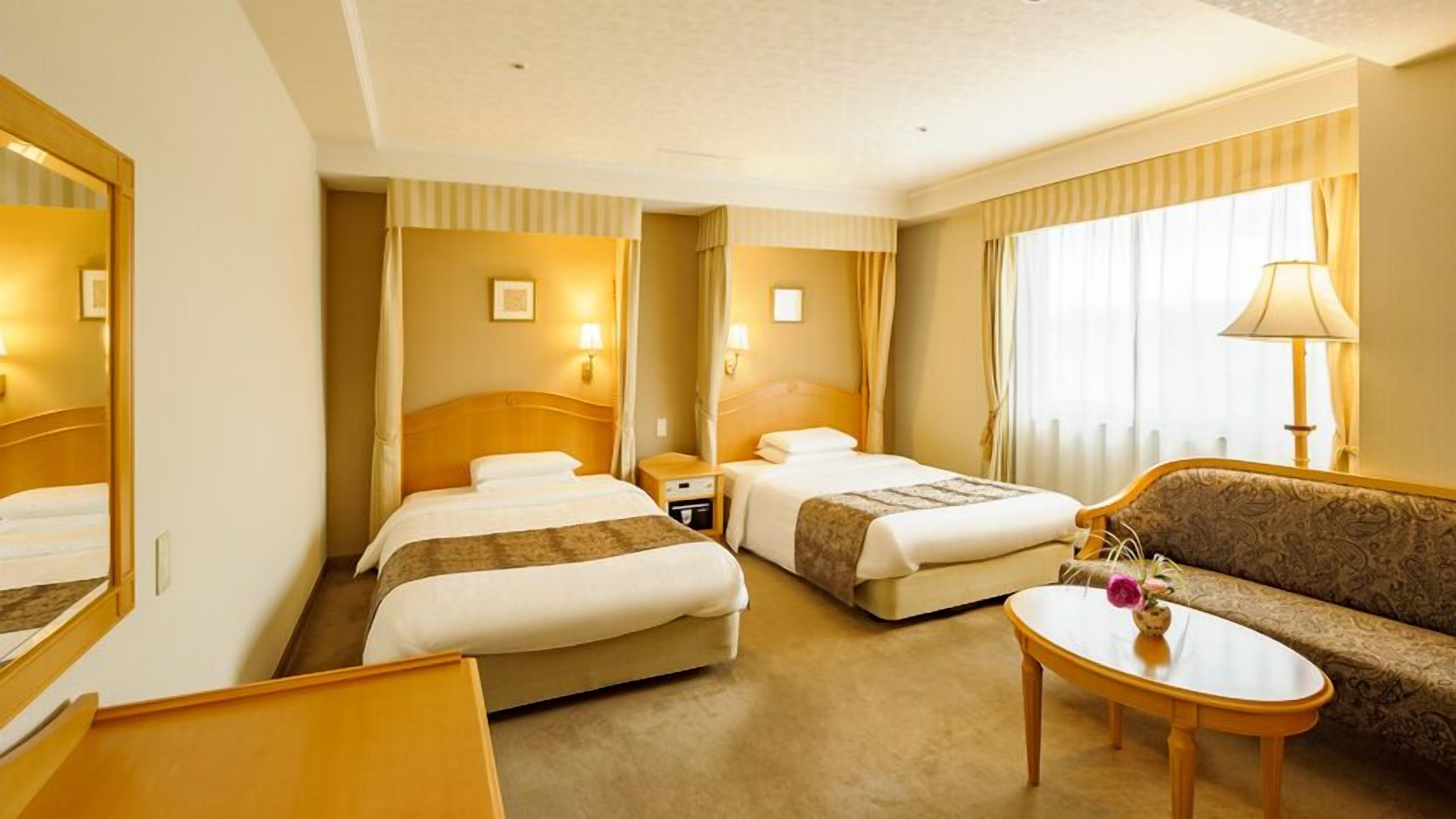 Een hotelkamer met twee bedden, een bank, een kleine tafel en een spiegel.