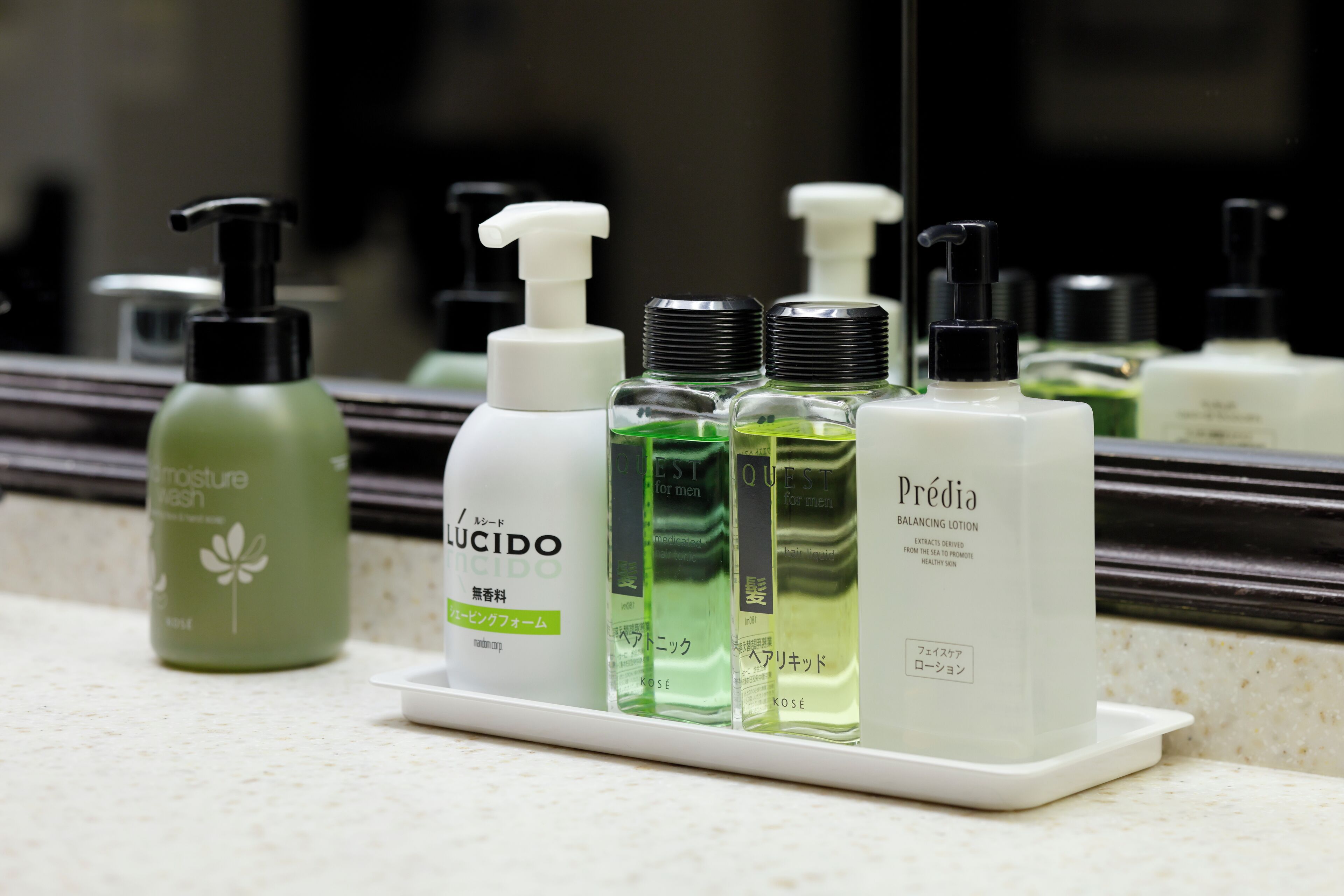 Una encimera de baño con diversos artículos de aseo, incluyendo una botella verde, una botella blanca con dispensador y otra botella blanca con dispensador.