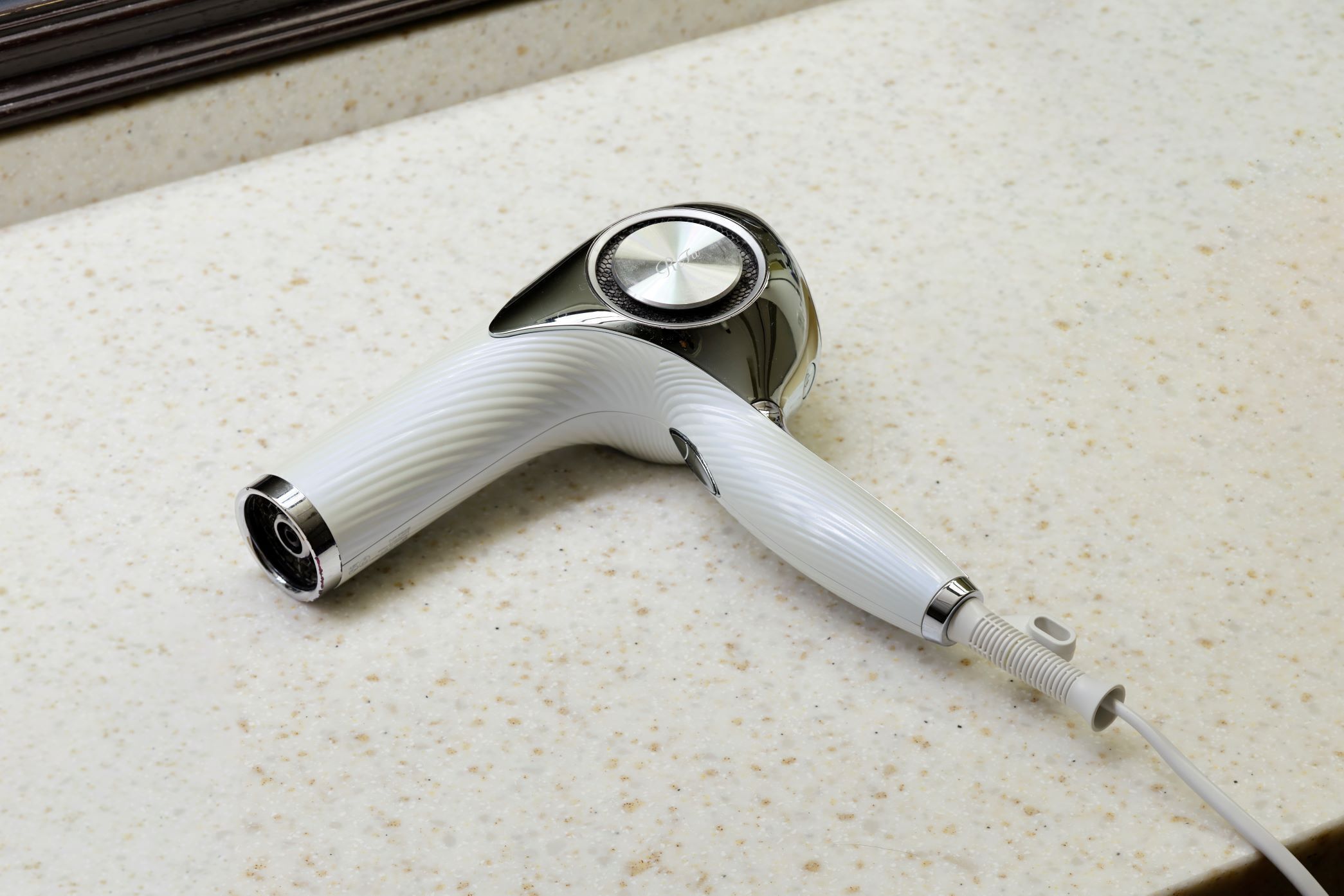 A hair dryer with a white handle and metallic base on a speckled countertop.