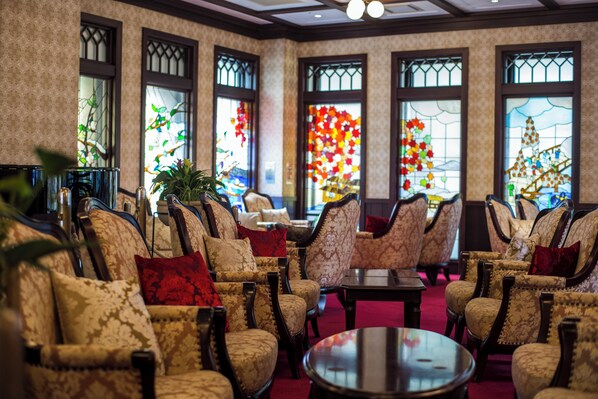 A hotel lobby with patterned armchairs, a central round table, and large windows with decorative glass panes. - Kanazawa Hakuchoro Hotel Sanraku (Kanazawa)