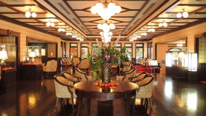 A spacious lobby with a central round table surrounded by chairs, a chandelier, and a large vase with flowers.