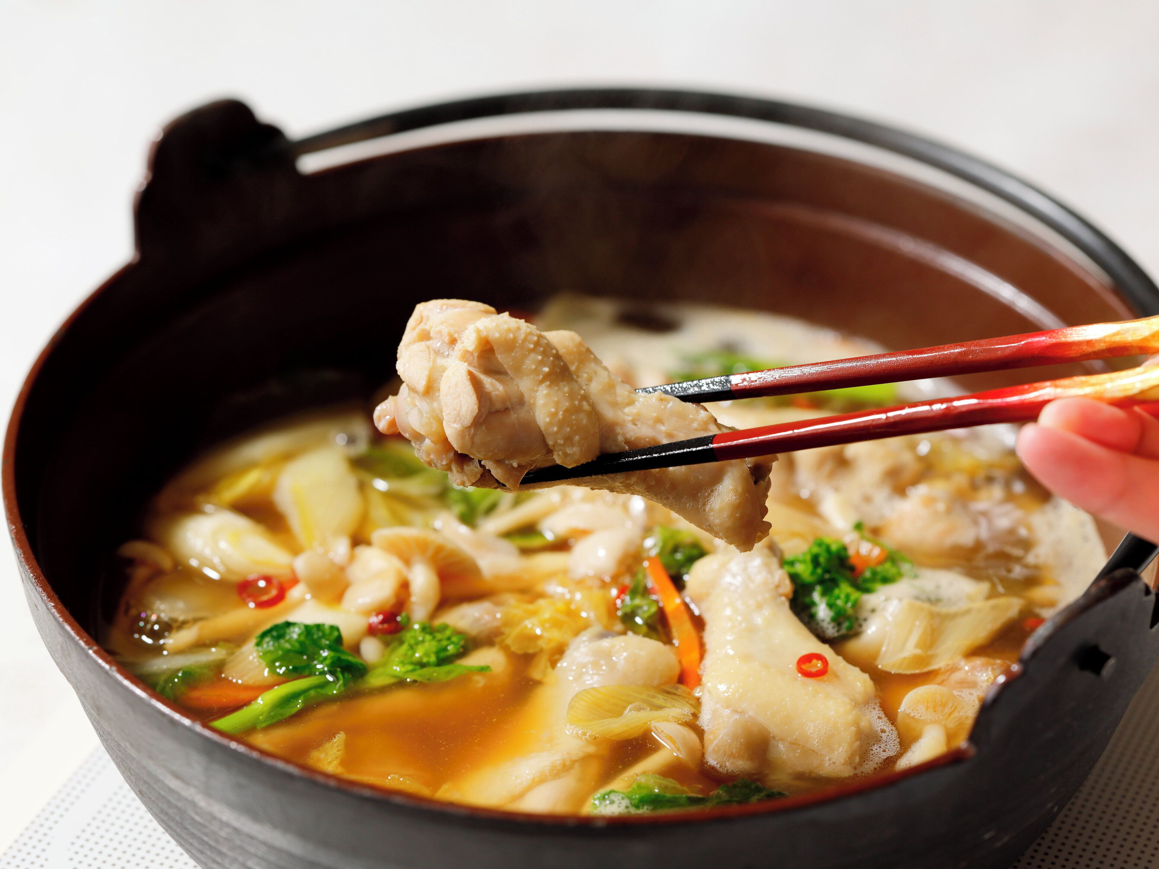 Eine Schüssel Suppe mit Nudeln und Gemüse, gehalten mit Essstäbchen.
