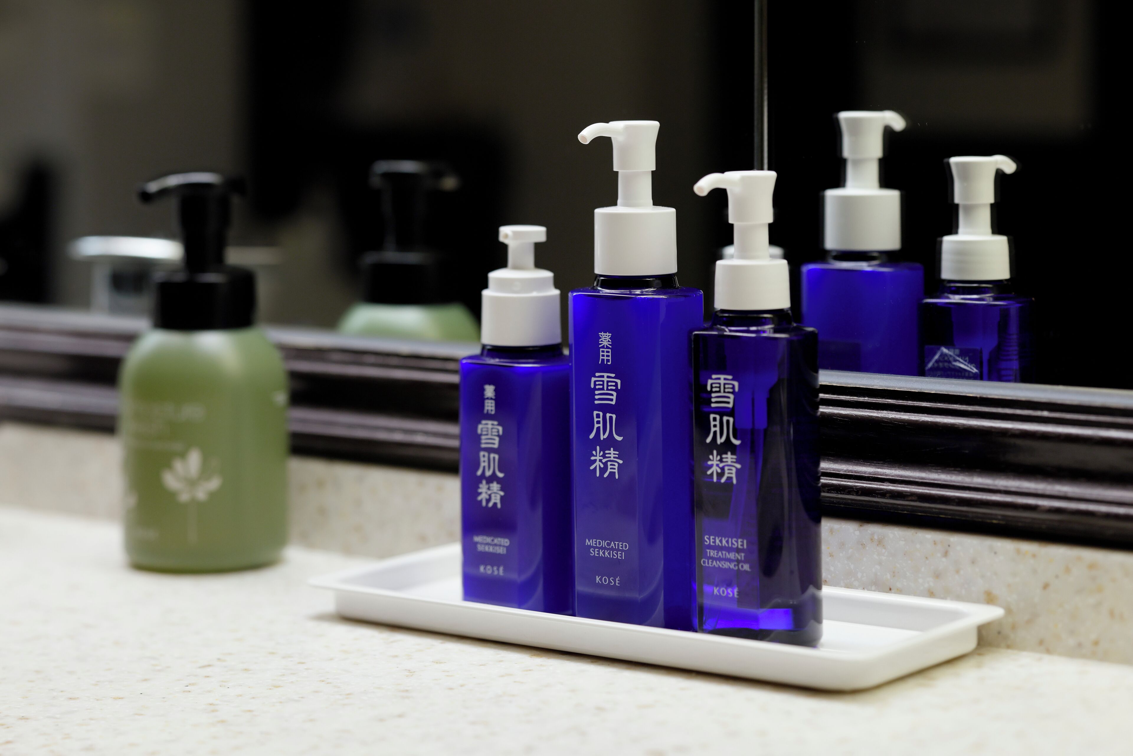 A bathroom counter with a white soap dish holding several bottles of skincare products.