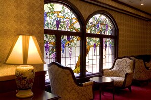A room with a lamp, two armchairs, a small table, and a stained glass window with floral patterns. - Kanazawa Hakuchoro Hotel Sanraku (Kanazawa)