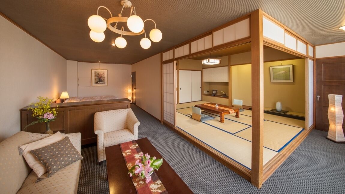 Une pièce de style japonais traditionnel, avec un sol recouvert de tatamis, une basse table en bois, un canapé et une porte coulissante donnant sur une autre pièce également recouverte de tatamis.