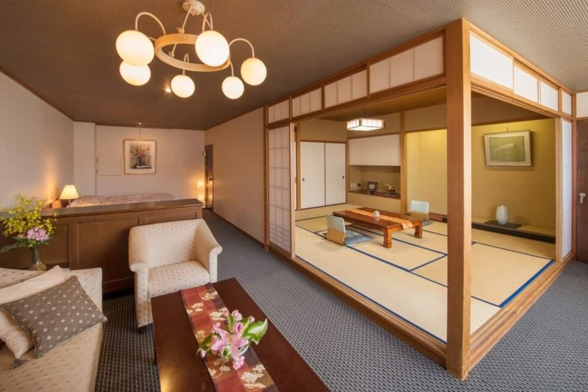 A traditional Japanese-style room with tatami flooring, a low wooden table, a sofa, and a sliding door leading to a tatami room.