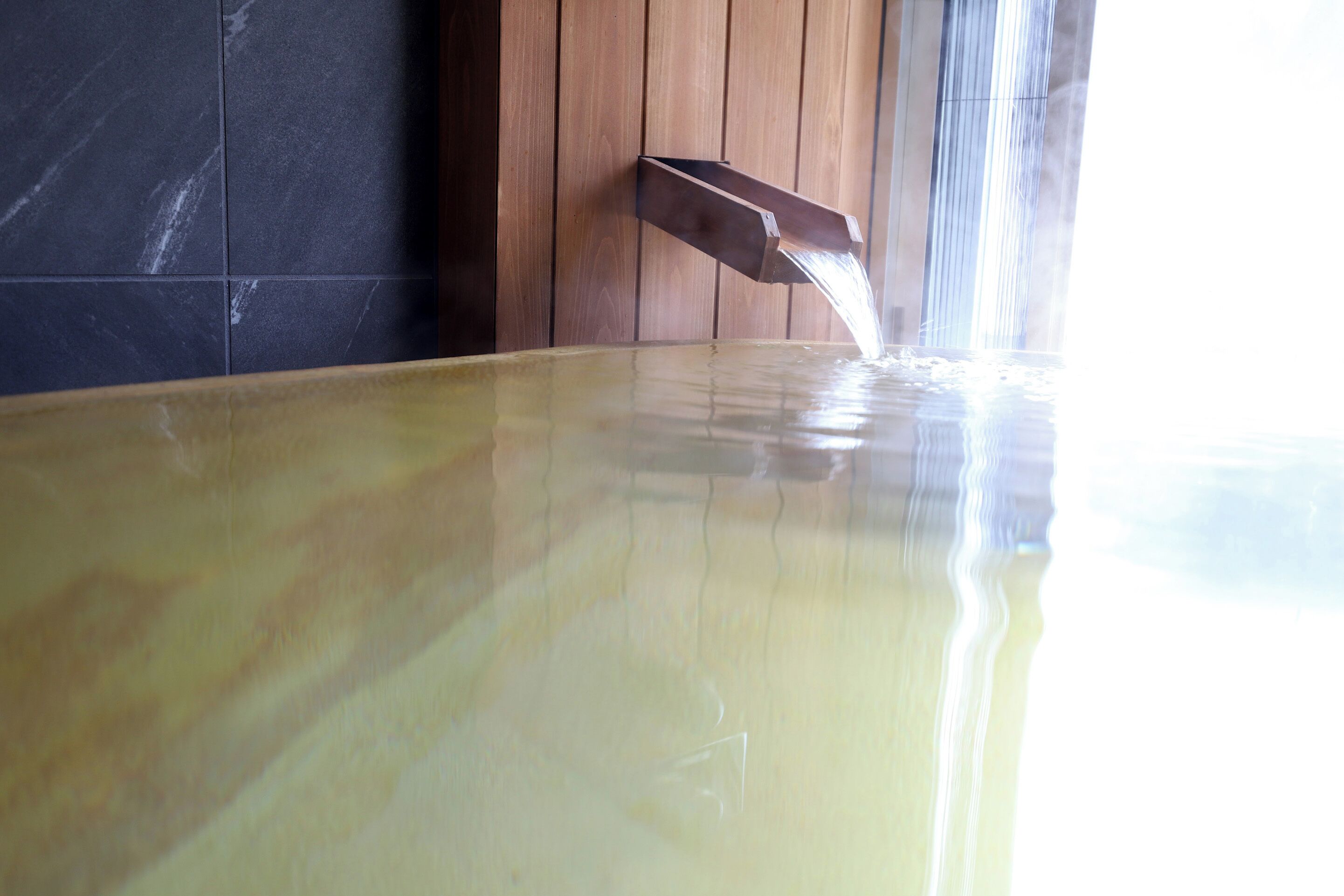 A hot tub with water flowing into it, set against a wooden wall and a tiled floor.
