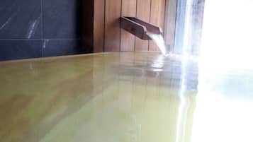 A hot tub with water flowing into it, set against a wooden wall and a tiled floor.