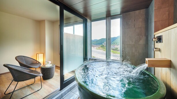 Une salle de bain moderne avec une grande baignoire, deux fauteuils en osier et une vue sur un paysage montagneux grâce à de grandes fenêtres.