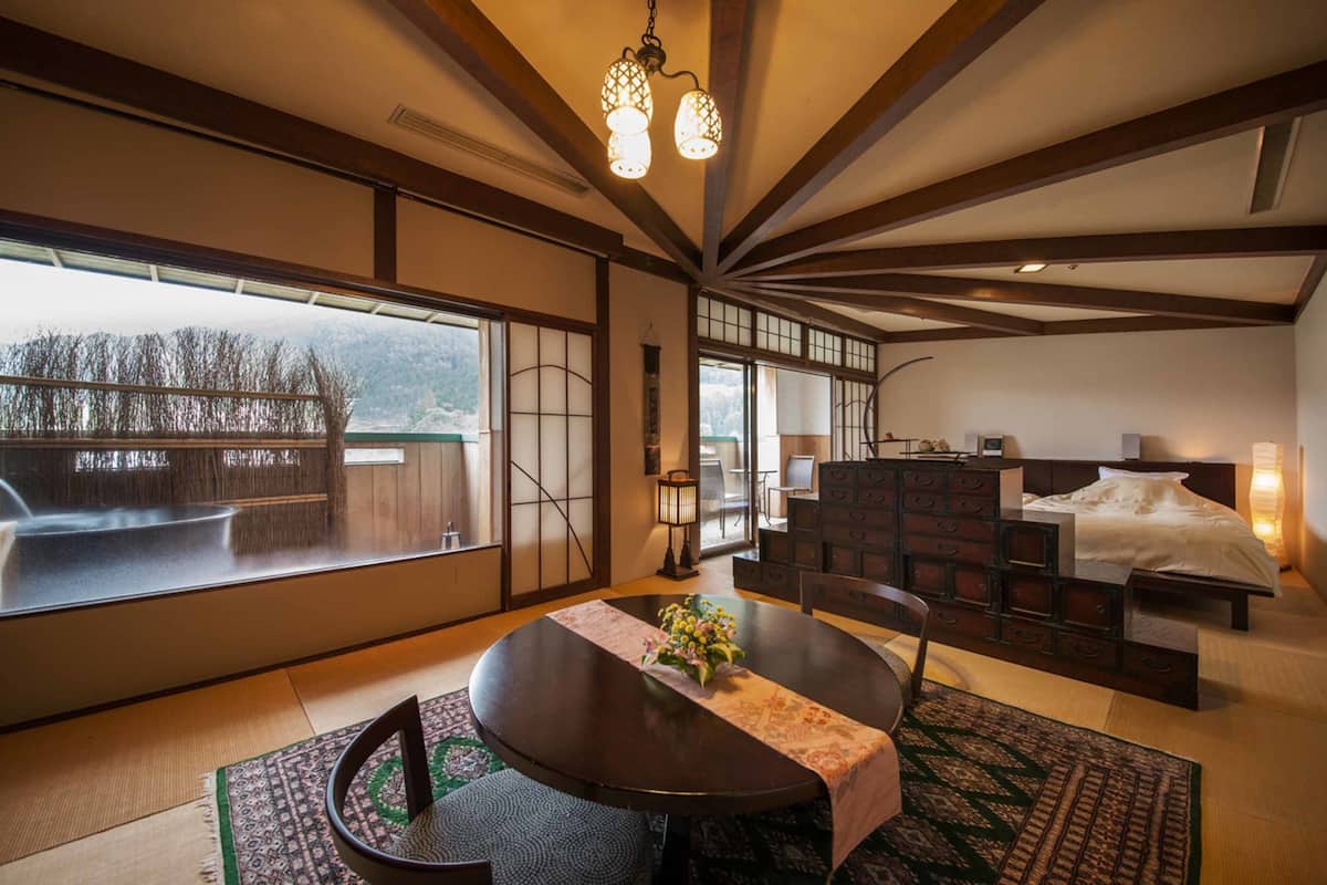 A traditional Japanese-style room with tatami flooring, a low wooden bed, and a dining area with a table and chairs.