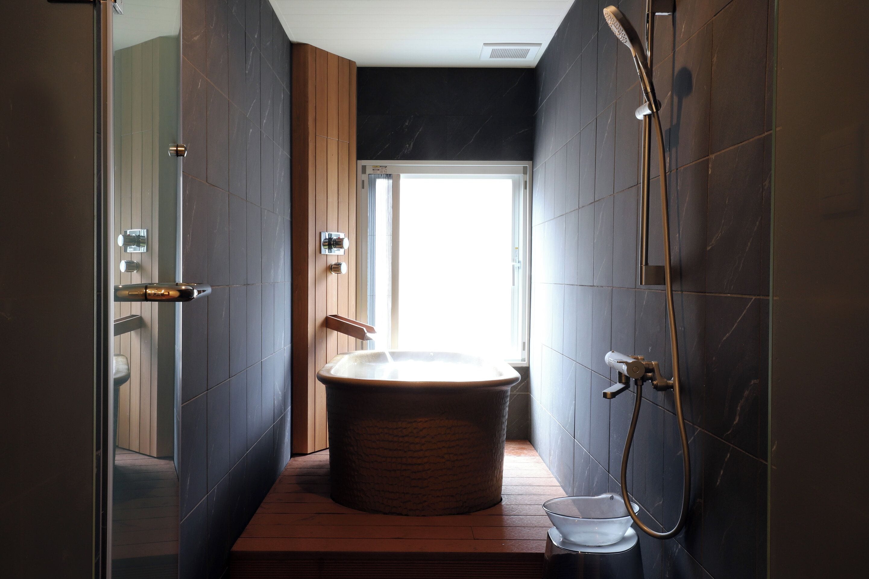 Een moderne badkamer met een vrijstaand bad, een douche en een glas water op de vloer.