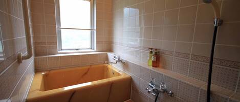 A bathroom with a bathtub, a window, a shower, and a sink.