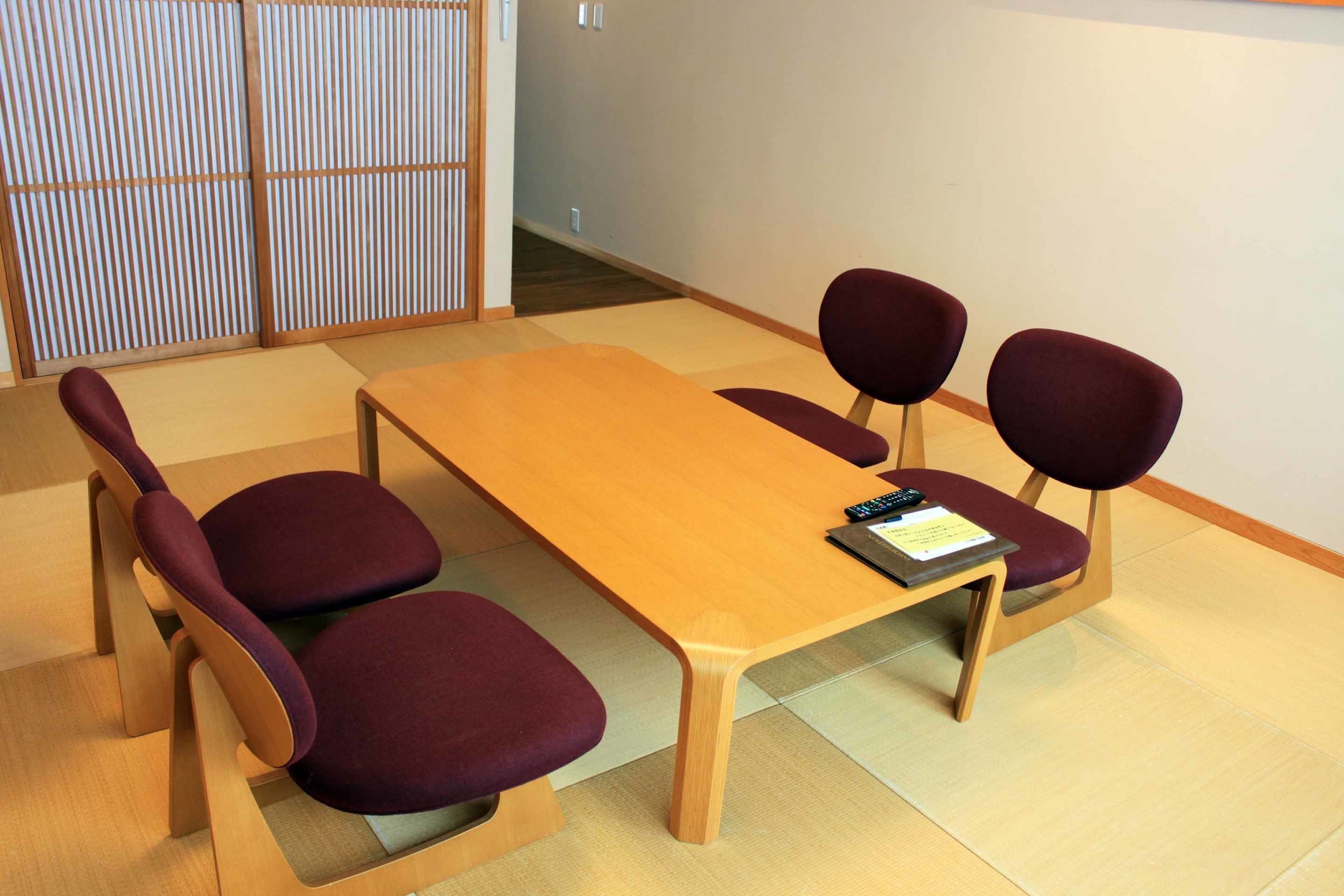 Een vergaderruimte met een houten tafel en vier paarse stoelen.