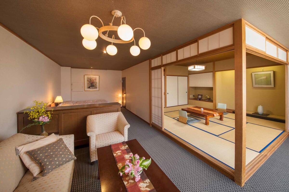 Ein traditioneller japanischer Raum mit Tatami-Böden, einem niedrigen Holztisch, einer Couch und einer hängenden Lampenleuchte.