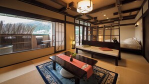Une pièce de style japonais traditionnel, avec un sol recouvert de tatamis, une table basse agrémentée d’un chemin de table rouge, un canapé avec des coussins et une grande fenêtre donnant sur l’extérieur.