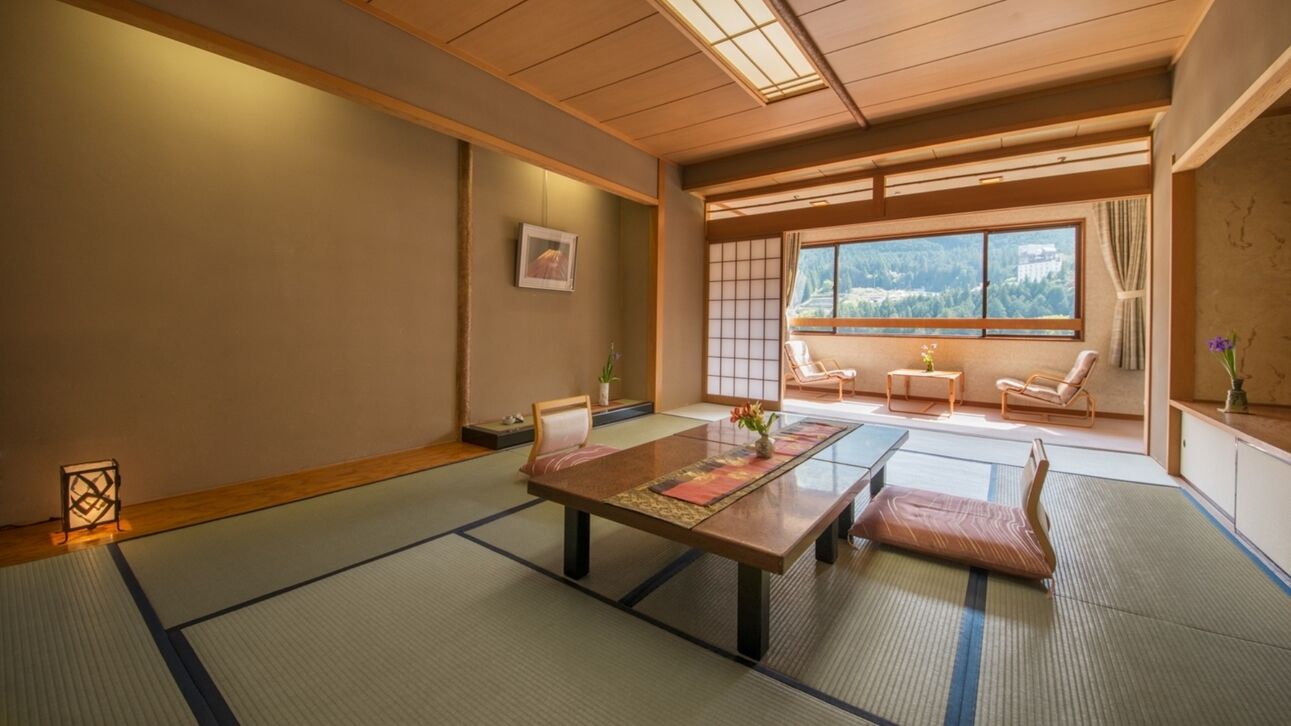 Une pièce de style japonais traditionnel, avec un sol recouvert de tatamis, une table basse et des portes coulissantes donnant sur un balcon avec vue.