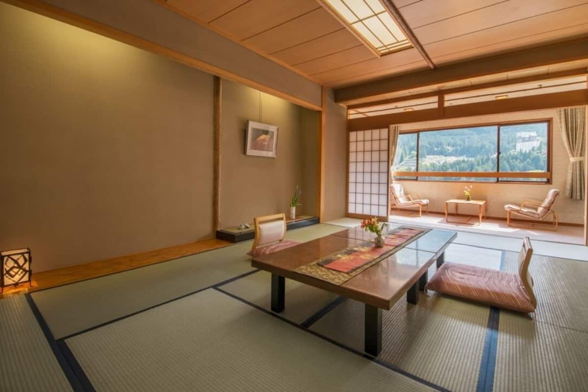 A traditional Japanese room with tatami flooring, a low table, and sliding doors leading to a balcony with a view.