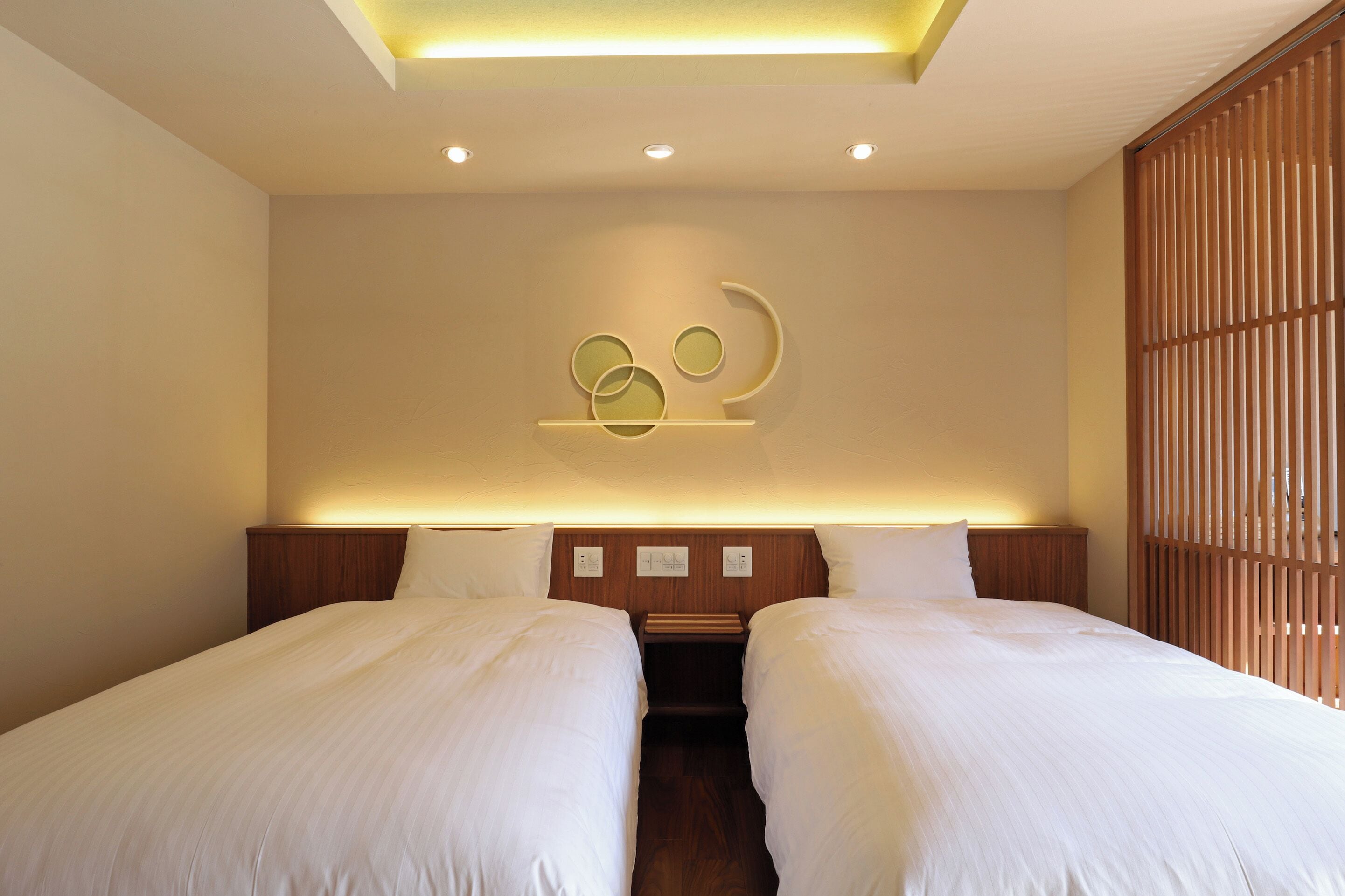 Habitación de hotel con dos camas, cabecera de madera, lámpara de pared y separador de madera.
